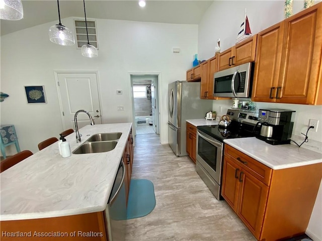 kitchen with a center island with sink, appliances with stainless steel finishes, brown cabinetry, and a sink