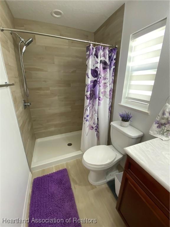 bathroom with vanity, wood finished floors, a tile shower, and toilet