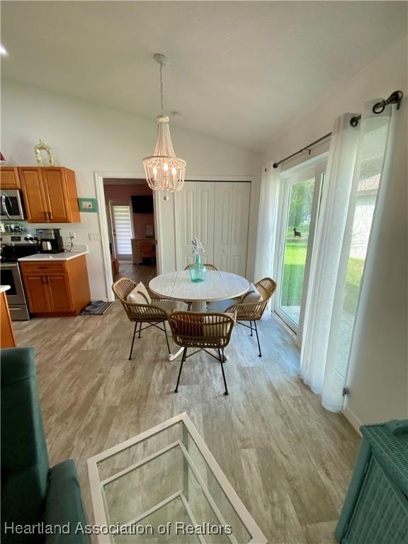 dining room with light wood finished floors, a chandelier, and vaulted ceiling