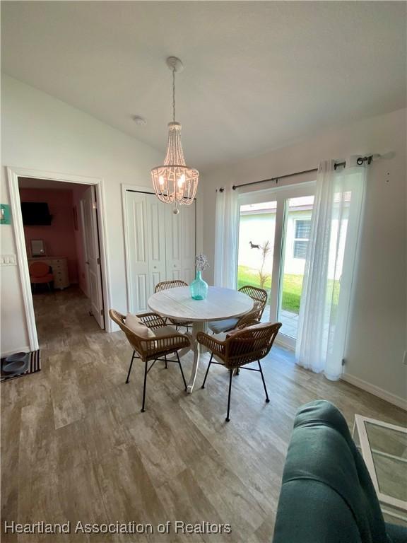 dining space featuring lofted ceiling, light wood finished floors, a chandelier, and baseboards