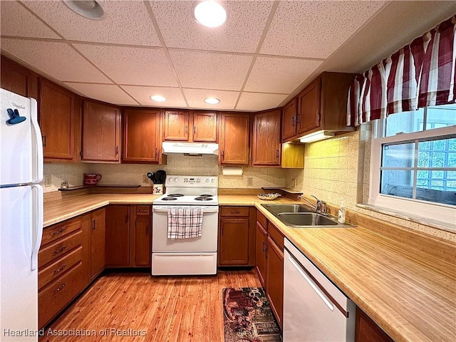 kitchen featuring white appliances, under cabinet range hood, a sink, and light countertops