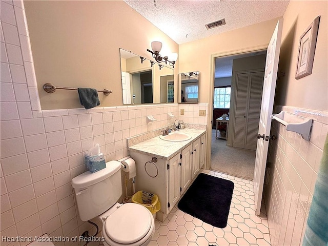 bathroom featuring visible vents, a textured ceiling, vanity, and tile walls
