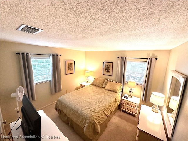 carpeted bedroom with a textured ceiling, visible vents, and multiple windows