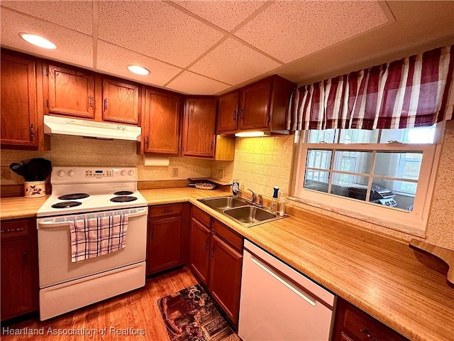kitchen featuring white appliances, light wood-type flooring, light countertops, under cabinet range hood, and a sink
