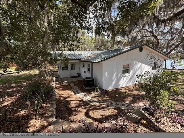 rear view of property featuring central air condition unit and metal roof
