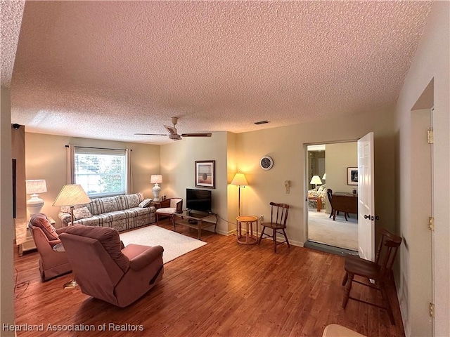 living room featuring a textured ceiling, baseboards, a ceiling fan, and wood finished floors