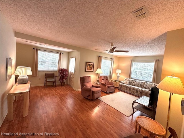 living room with a wealth of natural light, visible vents, wood finished floors, and a textured ceiling