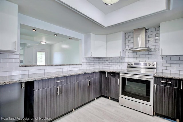 kitchen with decorative backsplash, light wood-style floors, wall chimney range hood, white cabinets, and stainless steel range with electric cooktop