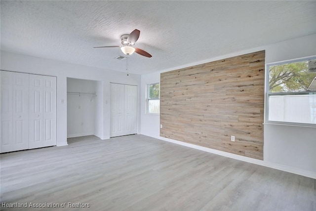 unfurnished bedroom featuring wooden walls, multiple closets, baseboards, wood finished floors, and visible vents