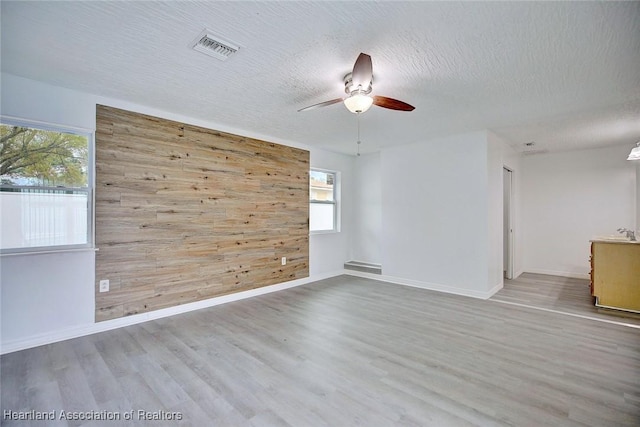 spare room featuring visible vents, ceiling fan, wood finished floors, and wooden walls