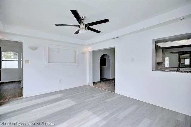 unfurnished living room with ceiling fan, arched walkways, baseboards, wood finished floors, and visible vents