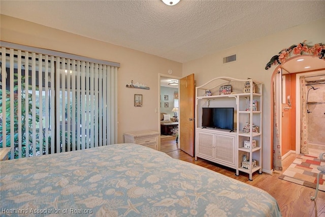 bedroom with a textured ceiling, light wood-type flooring, and ensuite bath