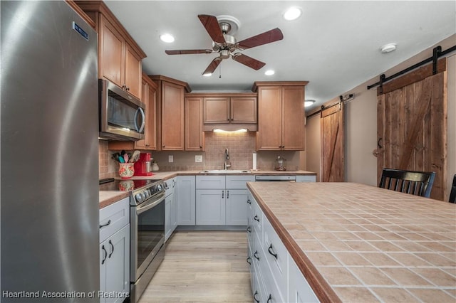 kitchen featuring stainless steel appliances, sink, a barn door, white cabinetry, and tile counters