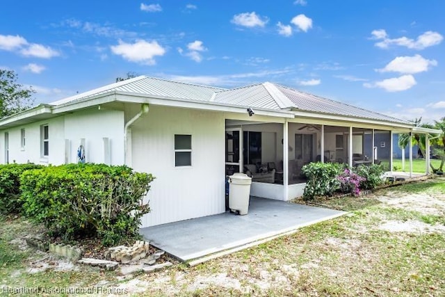 rear view of property featuring a sunroom, metal roof, and a patio