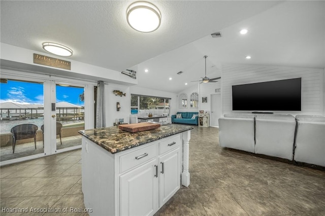 kitchen featuring a kitchen island, white cabinets, visible vents, a ceiling fan, and lofted ceiling
