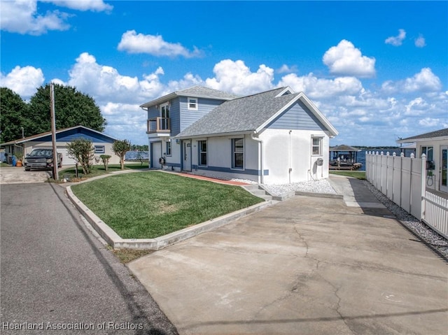 view of front of property with a front lawn, driveway, roof with shingles, stucco siding, and fence