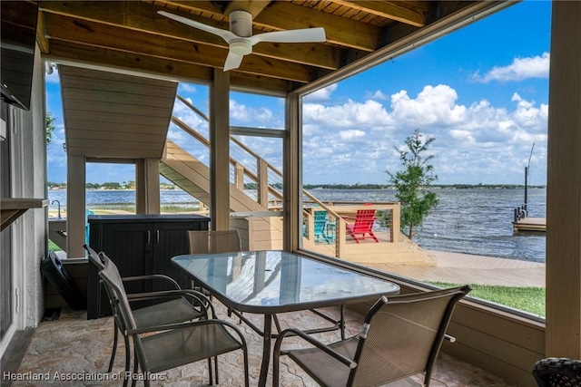 sunroom with ceiling fan, outdoor dining space, and a water view