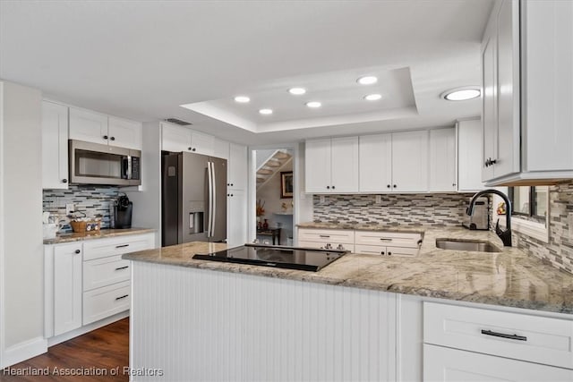 kitchen featuring a raised ceiling, white cabinetry, sink, and appliances with stainless steel finishes