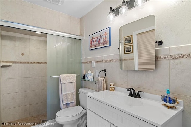 bathroom featuring vanity, toilet, a shower with shower door, and tile walls