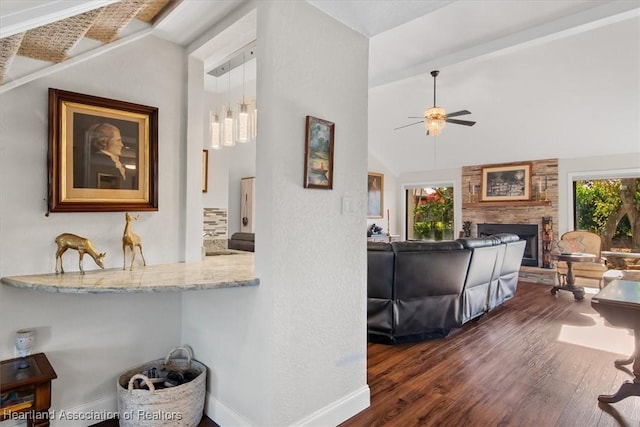 living room with a stone fireplace, ceiling fan, dark wood-type flooring, and a healthy amount of sunlight