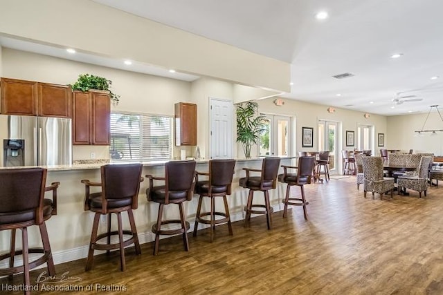 kitchen featuring ceiling fan, light stone countertops, dark wood-type flooring, stainless steel refrigerator with ice dispenser, and a kitchen bar