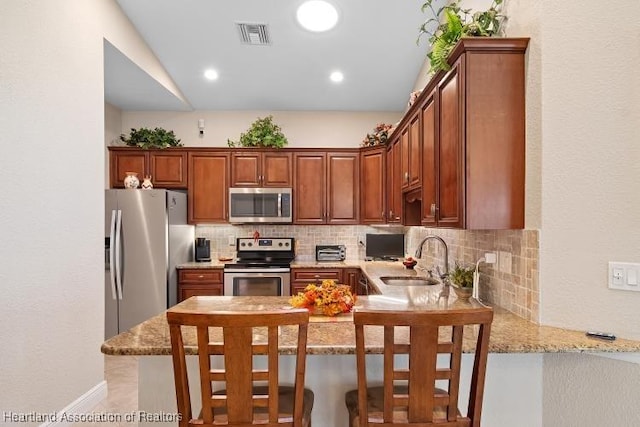 kitchen with kitchen peninsula, a kitchen bar, light stone countertops, stainless steel appliances, and sink