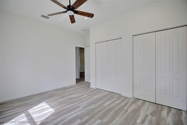 unfurnished bedroom featuring ceiling fan, light hardwood / wood-style flooring, and two closets