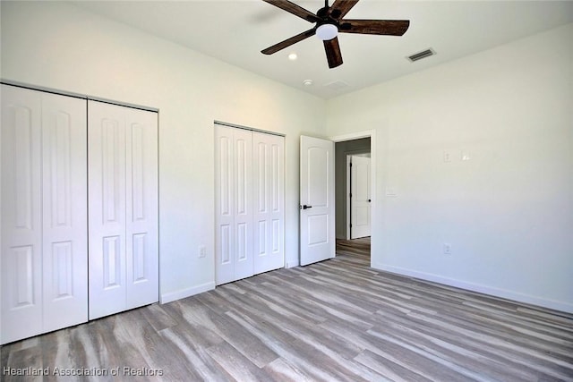 unfurnished bedroom with ceiling fan, two closets, and hardwood / wood-style flooring