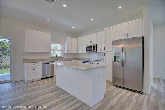 kitchen with white cabinets, appliances with stainless steel finishes, a center island, and light stone countertops