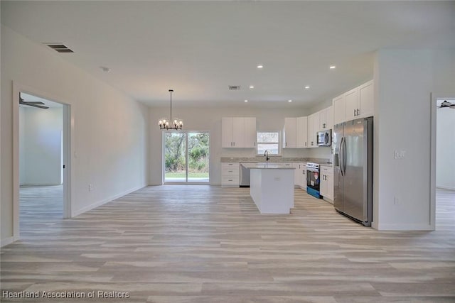 kitchen with a kitchen island, white cabinets, decorative light fixtures, and appliances with stainless steel finishes