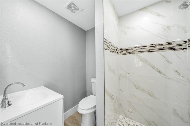 bathroom with a tile shower, hardwood / wood-style flooring, vanity, and toilet