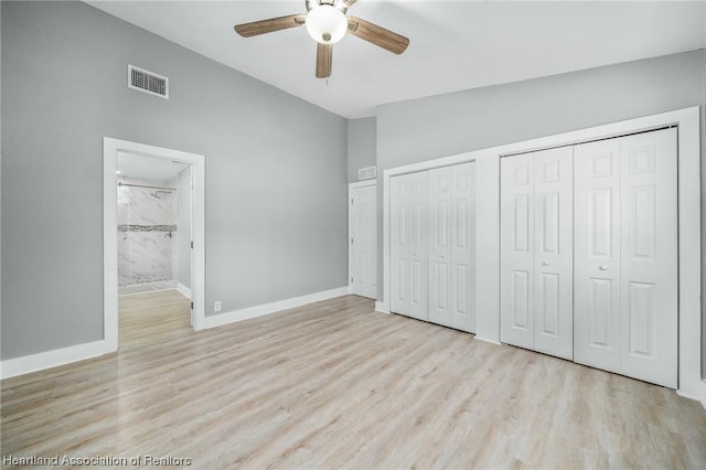 unfurnished bedroom with lofted ceiling, ensuite bath, light hardwood / wood-style flooring, ceiling fan, and multiple closets