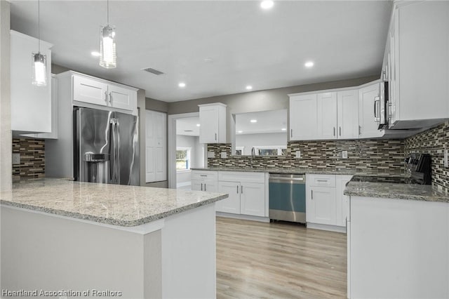 kitchen featuring kitchen peninsula, appliances with stainless steel finishes, light stone countertops, pendant lighting, and white cabinets