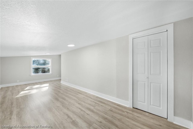 empty room with lofted ceiling, light hardwood / wood-style floors, and a textured ceiling