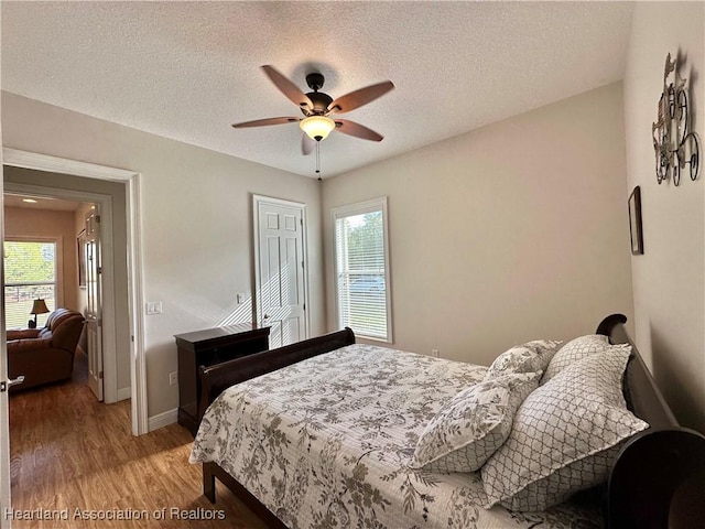 bedroom featuring ceiling fan, wood-type flooring, a textured ceiling, and multiple windows