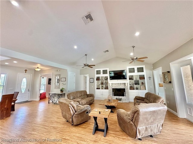 living room with ceiling fan, a stone fireplace, built in features, lofted ceiling, and light wood-type flooring