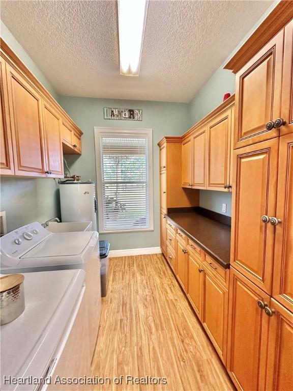 laundry room featuring cabinets, a textured ceiling, water heater, light hardwood / wood-style floors, and washing machine and clothes dryer