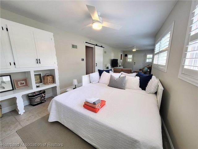 bedroom with ceiling fan, a barn door, and light tile patterned floors