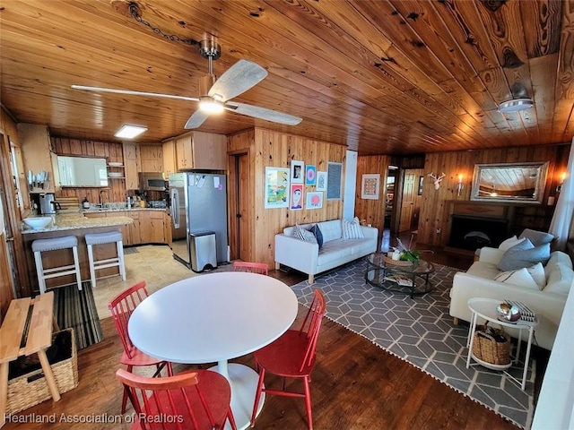 dining area with ceiling fan, wooden ceiling, sink, and wooden walls