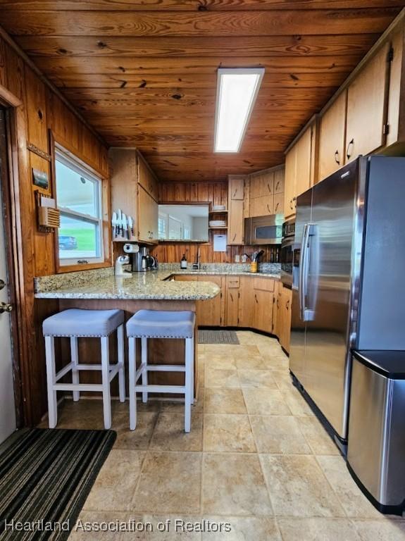 kitchen featuring kitchen peninsula, stainless steel appliances, light stone counters, and wood ceiling