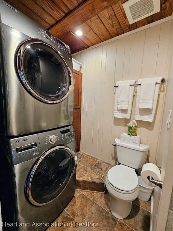 clothes washing area with wood ceiling, wooden walls, and stacked washing maching and dryer