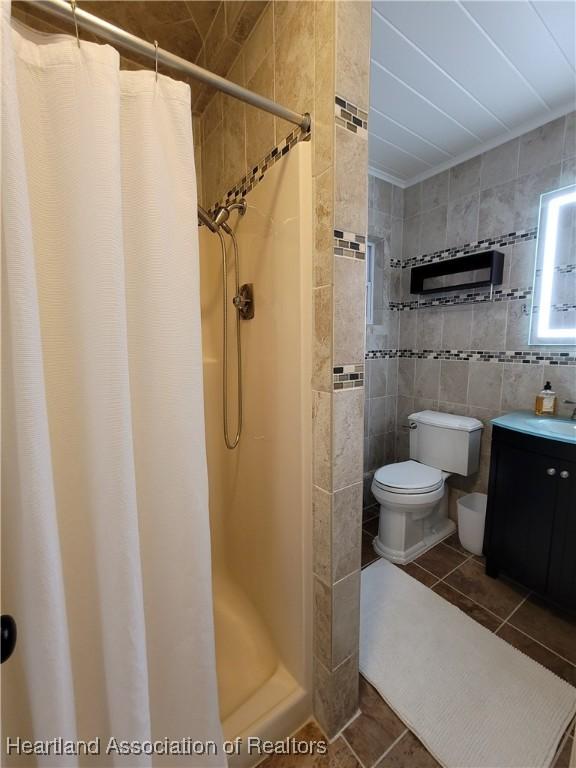 bathroom with tile patterned floors, toilet, vanity, tile walls, and a shower with shower curtain