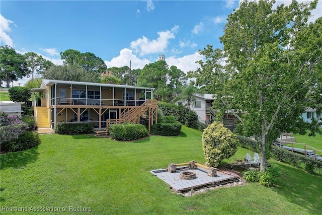 back of house with a sunroom, a fire pit, a deck, and a lawn