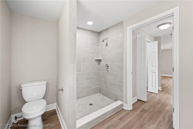 bathroom with hardwood / wood-style floors, a tile shower, and toilet