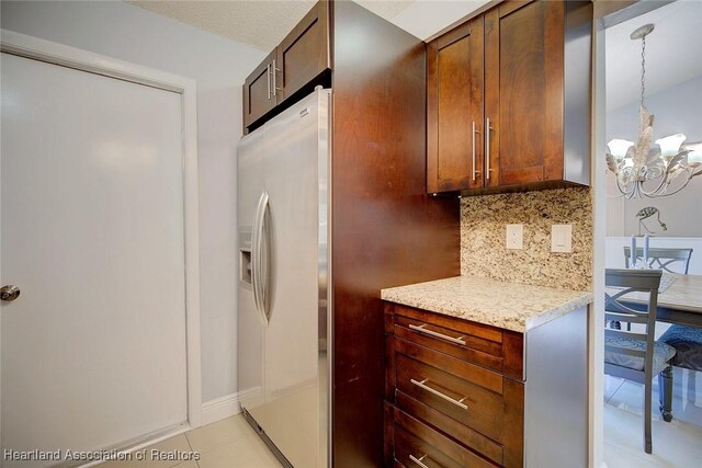 kitchen with light tile patterned floors, light stone counters, a notable chandelier, fridge with ice dispenser, and decorative backsplash