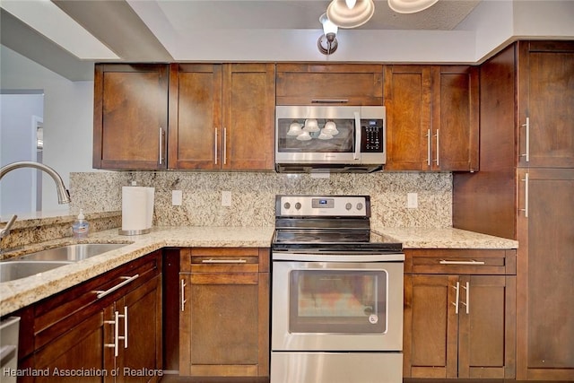 kitchen featuring appliances with stainless steel finishes, a sink, backsplash, and light stone counters