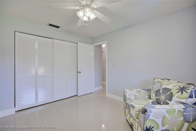 living area featuring light tile patterned floors, baseboards, visible vents, ceiling fan, and a textured ceiling