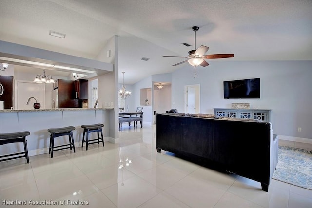 living area featuring lofted ceiling, light tile patterned flooring, ceiling fan with notable chandelier, visible vents, and baseboards