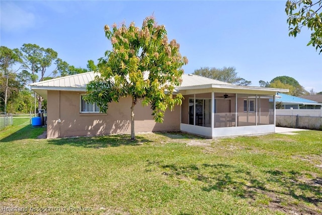 rear view of property with a sunroom, fence, metal roof, and a yard