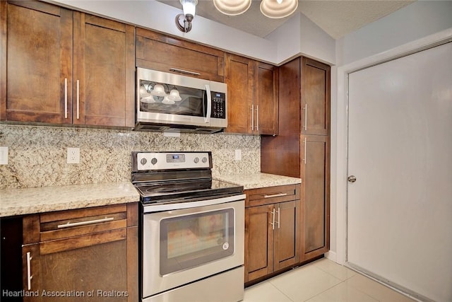 kitchen with light tile patterned floors, a textured ceiling, stainless steel appliances, backsplash, and light stone countertops